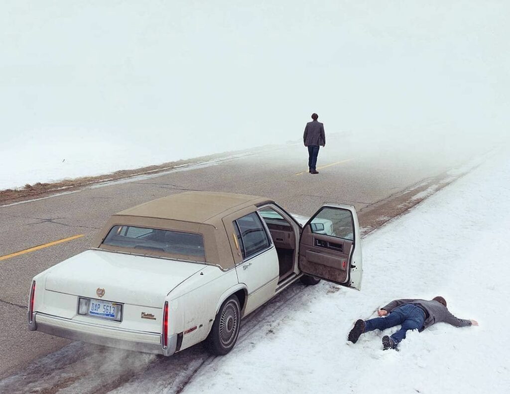 Logan Zillmer man lying face down in snow beside car hiver neige face contre terre