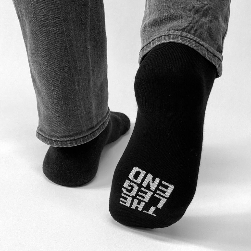 le dessous d'une chaussette noire sur laquelle est inscrit en blanc "the Leg End"
