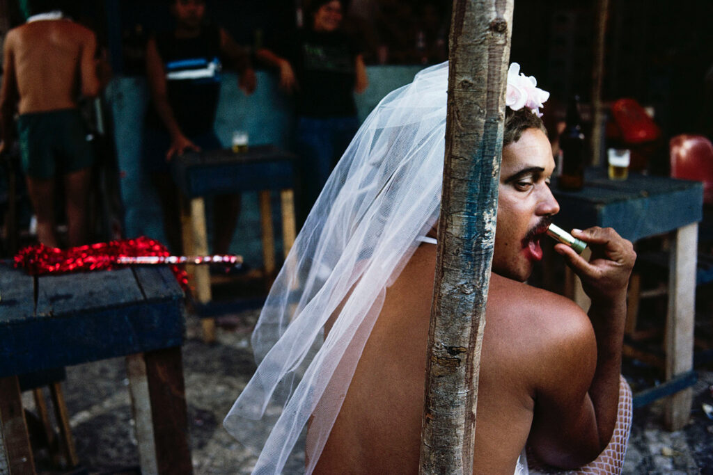 un homme moustachu en robe de mariée applique du rouge sur ses lèvres