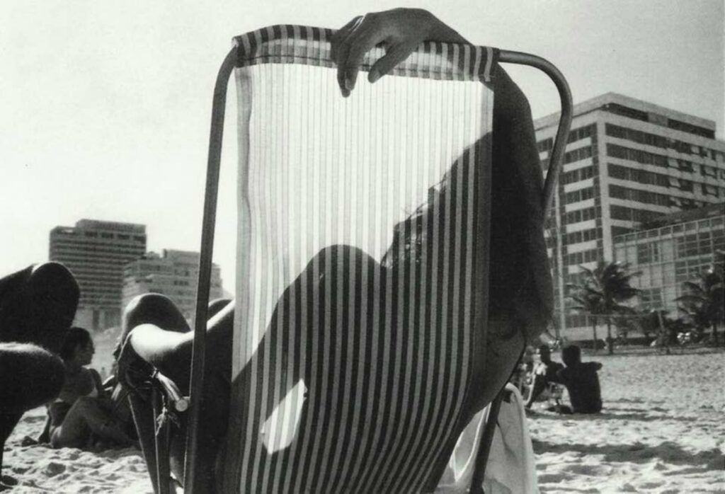 au travers de la toile aux rayures de zèbre d'un transat, une femme allongée sur la plage