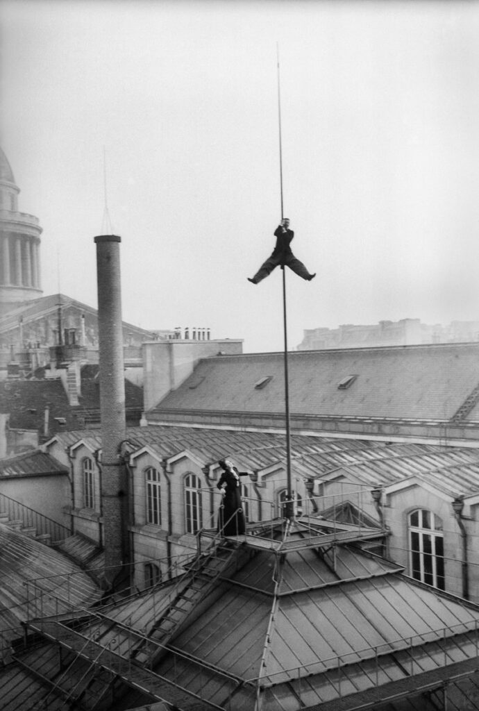 Henri Roger (1869-1946), photographe français, grimpant au paratonnerre de l'Ecole de Droit le jour des ses fiançailles avec Jeanne Viollet en bas . Paris, 10 décembre 1899.