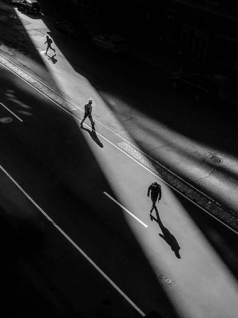 en ville, un rayon de soleil entre les immeubles dessine un couloir sur la chaussée, trois hommes l'empruntent comme un passage piétons