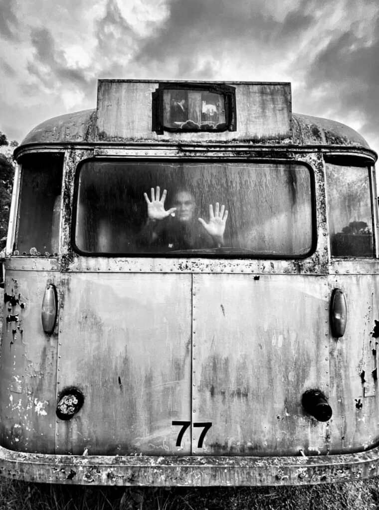 un homme dans l'épave d'un bus,  les mains appuyées sur la vitre arrière