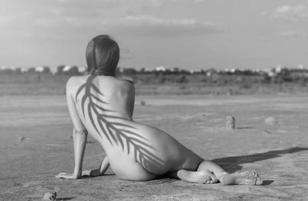une femme nue assise sur la plage, l'ombre d'une colonne vertébrale végétale dans le dos