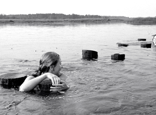 une femme se baigne sur les Deux Plateaux, dans la cour d'honneur du Palais-Royal à Paris, en France, souriant contre l'aversité, s'accrochant aux colonnes de Daniel Buren, presque submergées par la pluie