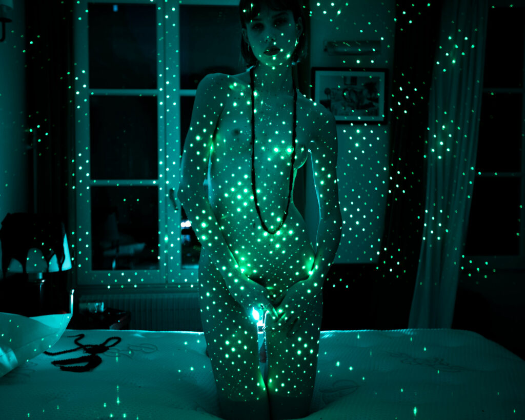 la nuit, à genoux sur le lit, une femme nue derrière un rideau de lumière