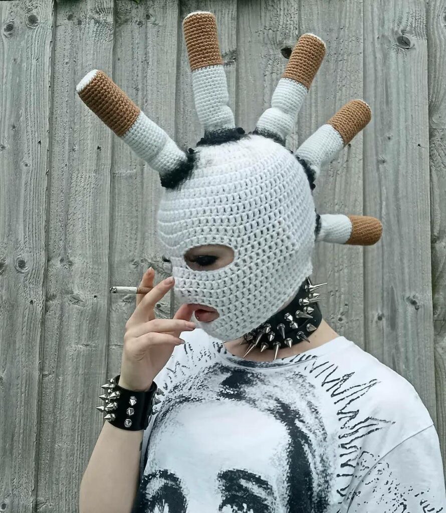 jeune femme portant un collier à clous et une cagoule cendrier sur laquelle des cigarettes écrasées sont artistiquement disposées en crète 