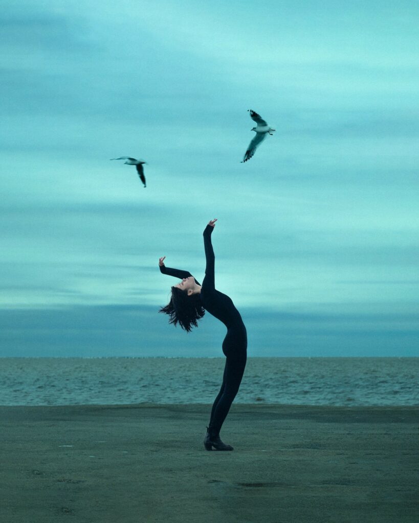 sur la plage bleue le corps de la femme en noir fait écho aux mouvements des oiseaux