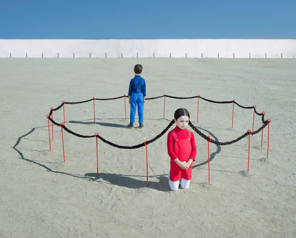 sur la plage, un jeune garçon dans son parc délimité par les nattes d'une petite fille