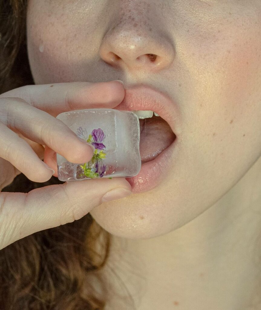 une femme porte à sa bouche un glaçon contenant une petite fleur mauve