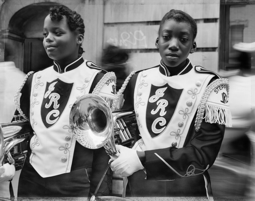 deux jeunes musiciennes noires d'une fanfare à Harlem, en tenue de défilé, leur instrument à vent sous le bras