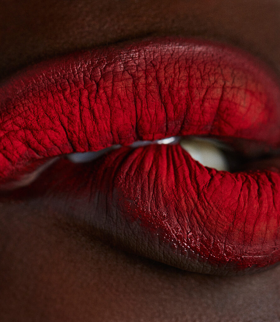 la texture au plissé floral de lèvres d'un rouge profond dont l'inférieure  est tenue entre les dents