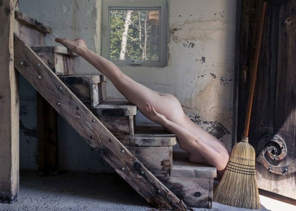 une femme nue, allongée la tête en bas sur les marches de l'escalier, la tête cachée par un balai