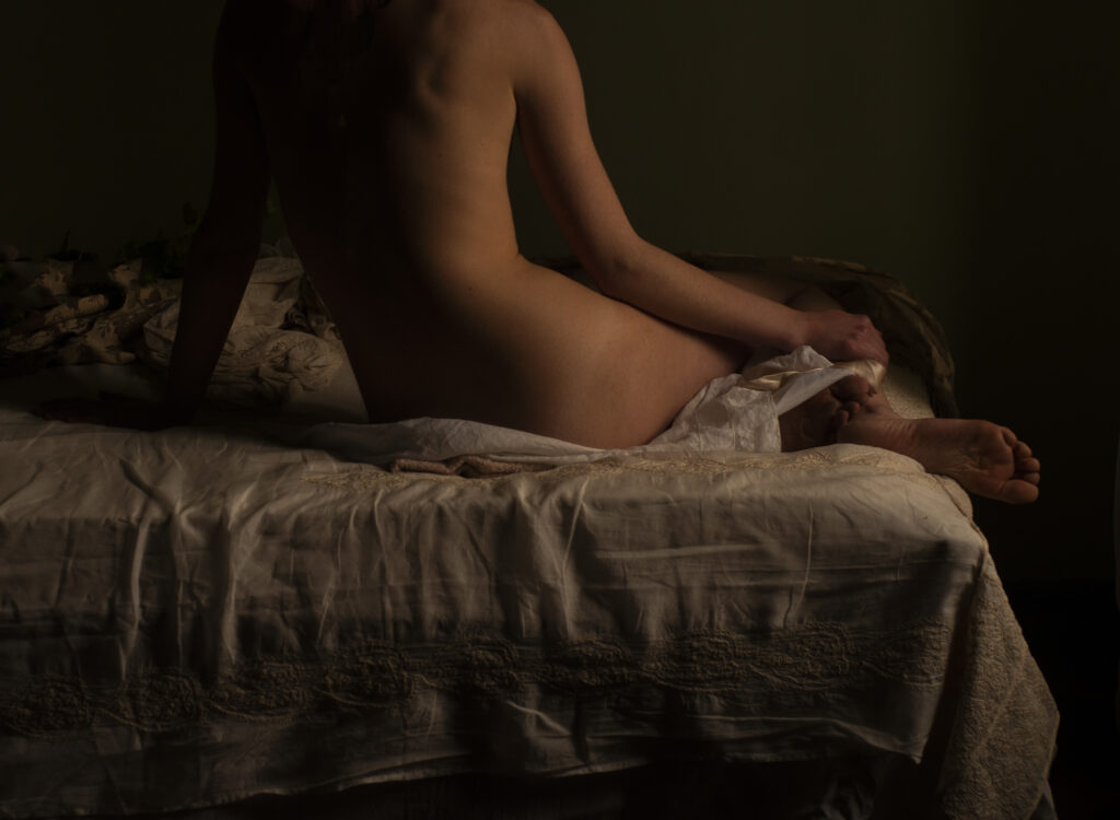 le dos d'une femme nue assise sur son lit dans la lumière douce du matin