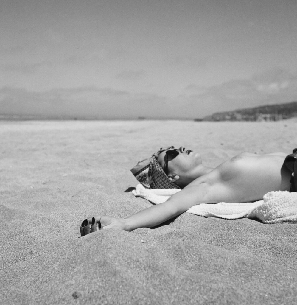 sur la plage immense, une femme allongée sur le dos, les bras en croix, seins nus