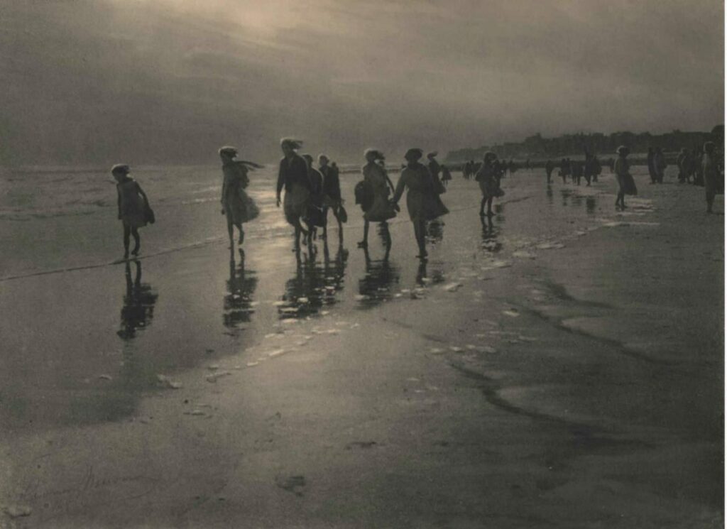 sous un ciel couvert, un groupe de femmes marchent sur la plage les pieds dans l'eau