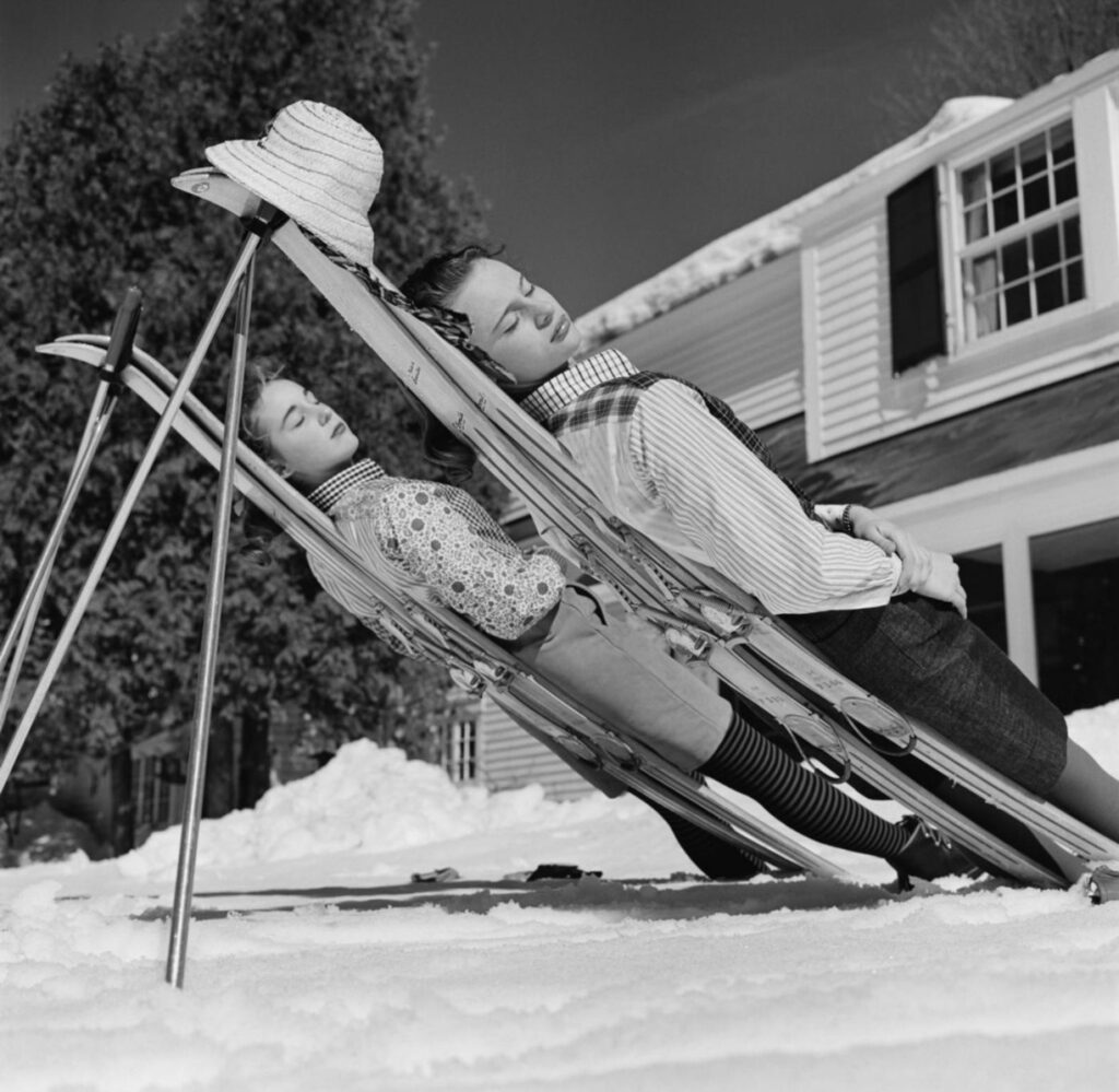 allongées comme sur un transat sur la semelle de leurs skis appuyés sur leurs bâtons, deux jeunes femmes prennent le soleil