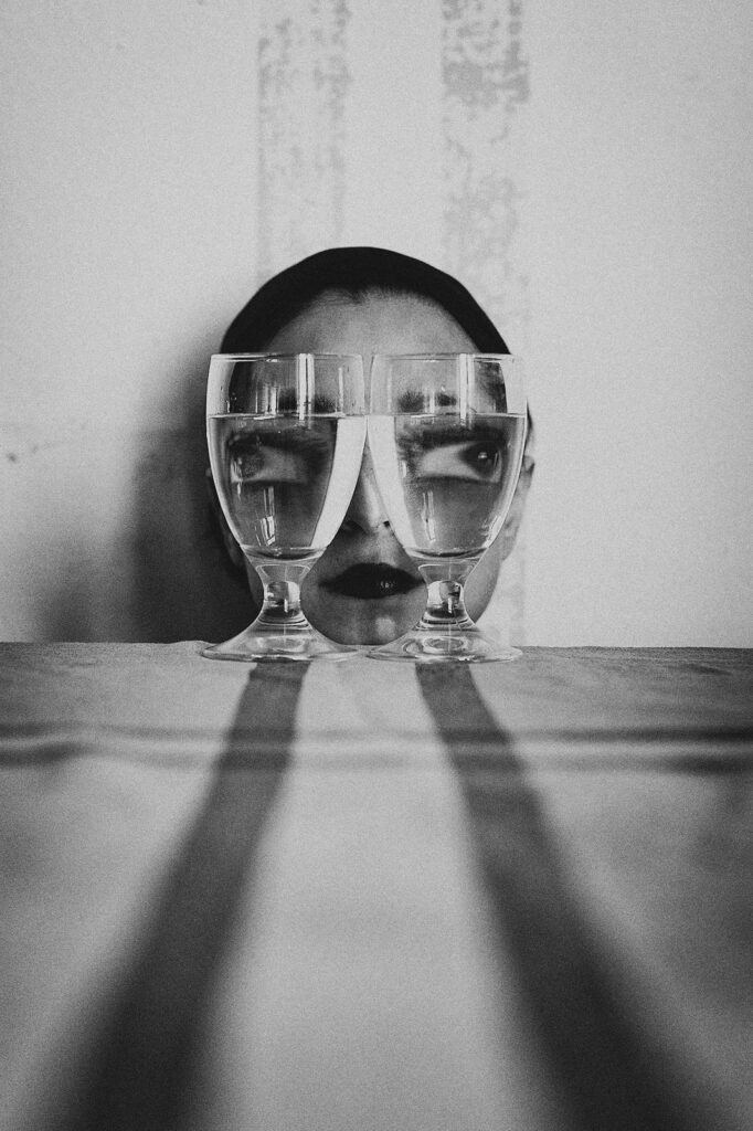 les yeux rendus globuleux par l'effet loupe grossissante de deux verres d'eau posés devant le visage d'une femme au bord d'une table