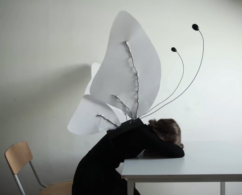 assise sur une chaise, une jeune femme en costume de papillon a posé sur la table sa tête sur ses bras croisés
