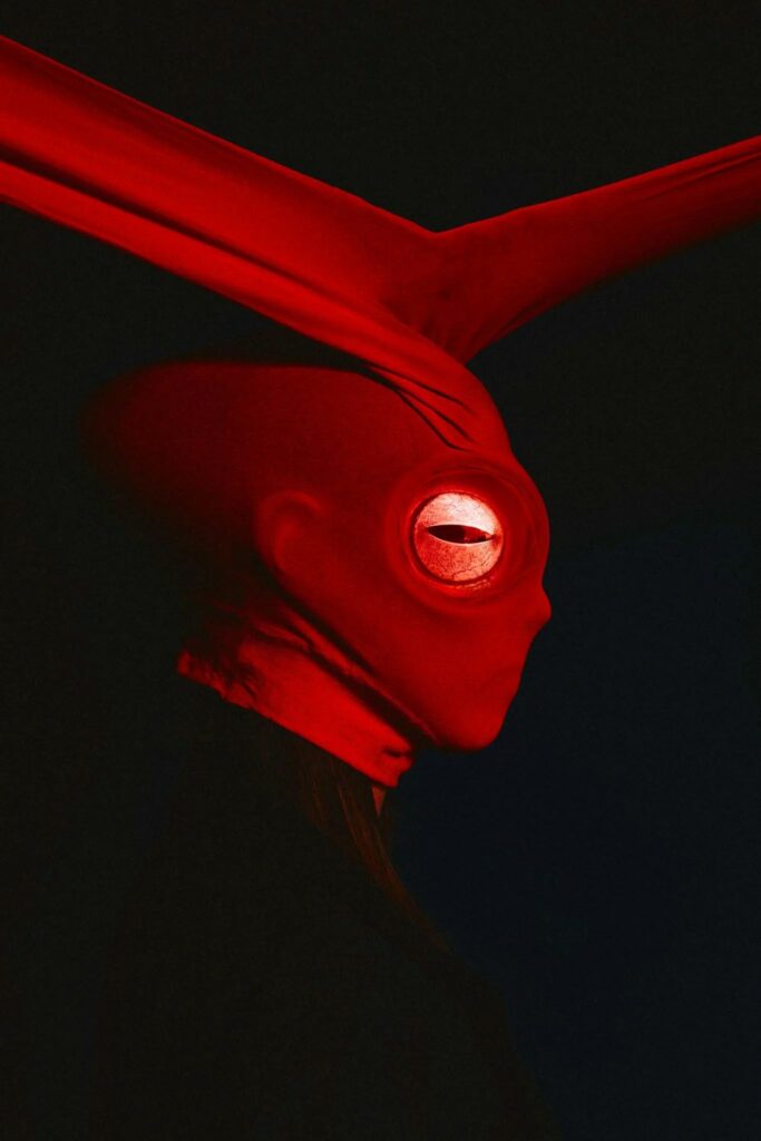 l'oeil dans une tête en ballon de rugby masquée par un collant rouge aux oreilles nouées sur le haut du crâne