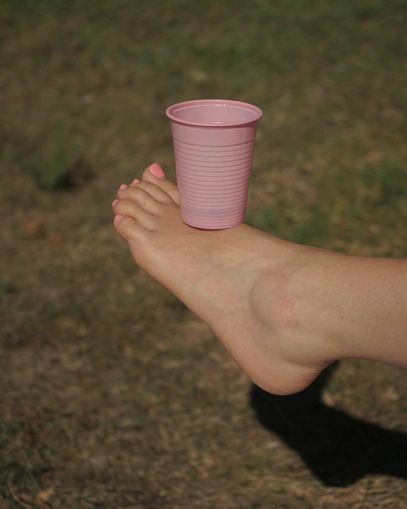 un gobelet rose en équilibre sur un  pied de femme aux ongles vernis assortis