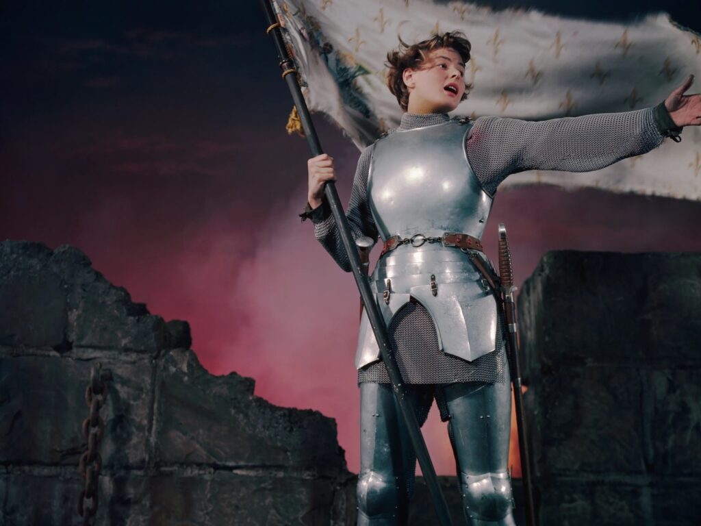 Jeanne d'Arc, en armure de chevalier, brandissant un étendard devant une muraille écroulée