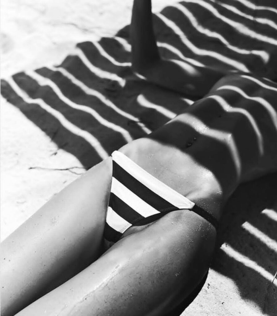 sur la plage, les rayures d'ombre générées par le dais l'abritant du soleil et celles du maillot de bain d'une femme allongée se confondent en un mirage