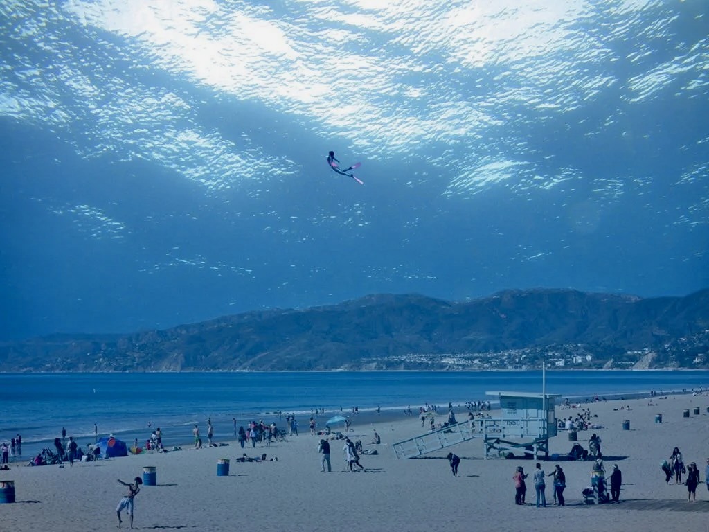 de la plage bleue, une femme s'élève avec ses palmes vers le ciel qui est la surface de la mer