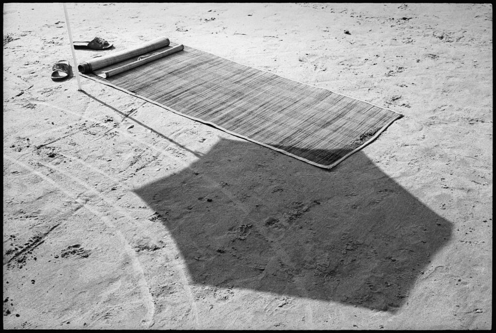 à côté de l'ombre d'un parasol, un tapis de plage semble flotter au dessus du sable