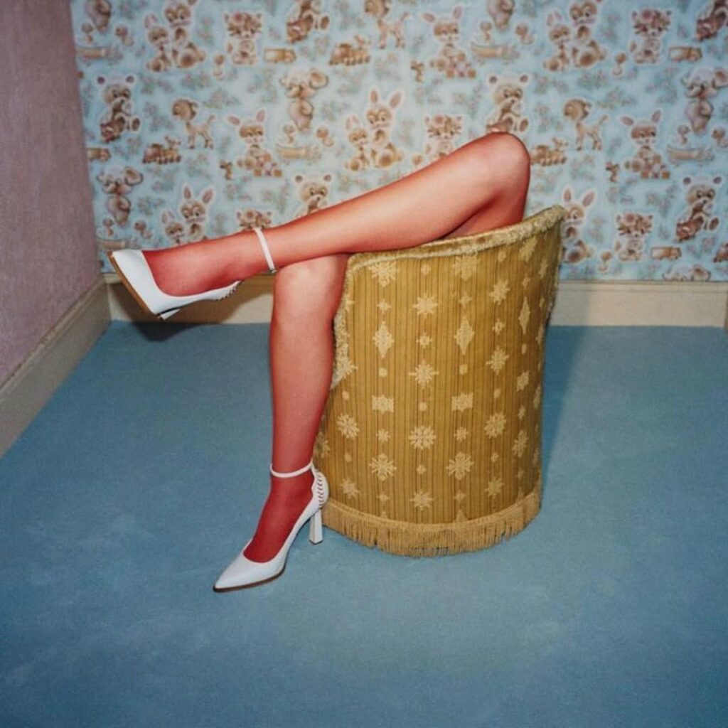 sur le dossier d'un fauteuil en osier, les jambes d'une femme chaussée de blancs souliers