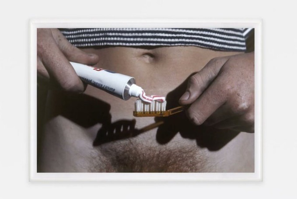 gros plan sur les mains d'une femme étalant de la pâte dentifrice sur sa brosse à dents entre son nombril surmonté d'un crop top à rayures et son pubis non épilé