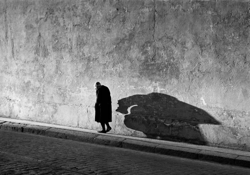 l'ombre sur un mur en forme de créature légendaire cracheuse de feu, gigantesque reptile ailé aux pattes griffues, d'un homme courbé marchant sur le trottoir
