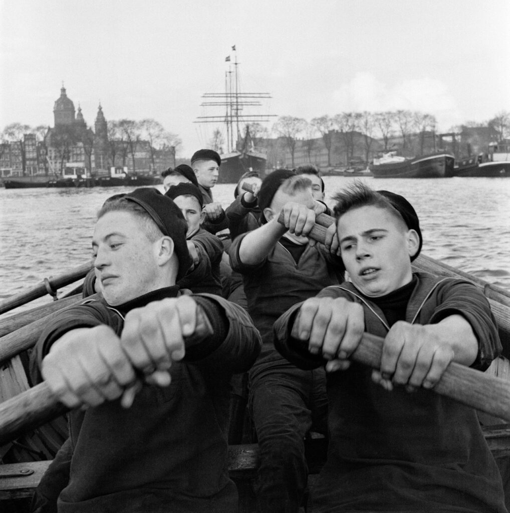 des marins tirant fortement et de façon coordonnée sur les avirons d'une barque dans le port