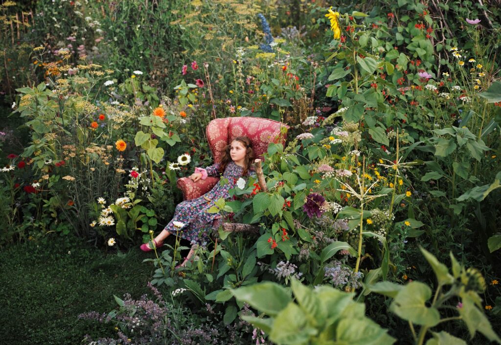 une jeune fille assise dans un fauteuil rose au coeur d'un jardin extraordinaire en fleurs