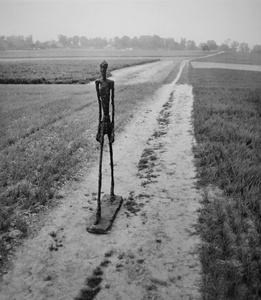 la sculpture d'un homme en marche  sur un chemin de campagne