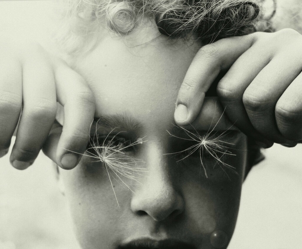 un jeune garçon tient de fins akènes à aigrettes (genre Taraxacum) blanches comme des flocons devant ses yeux