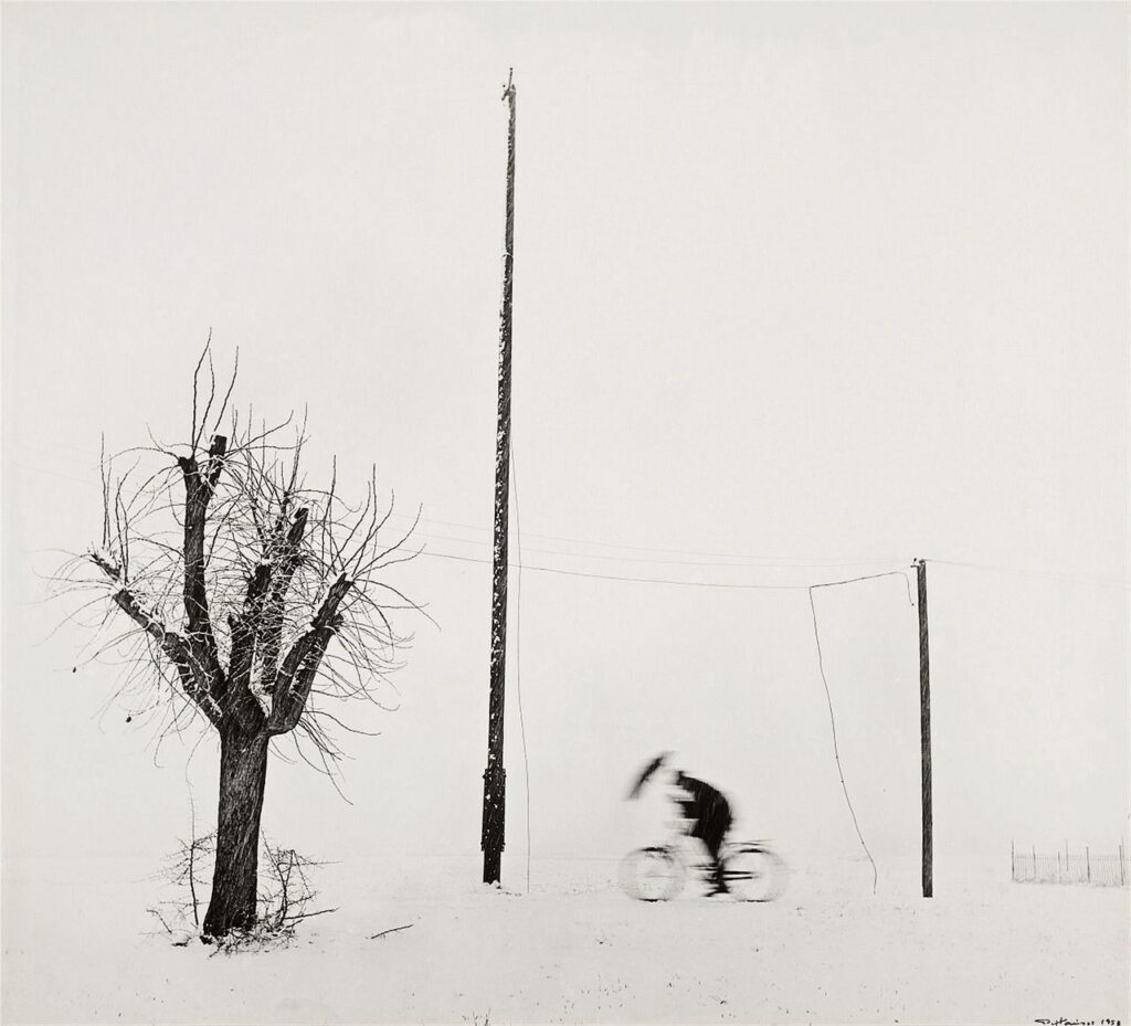 dans un paysage minimaliste d'hiver, un cycliste pédale avec son parapluie contre la neige