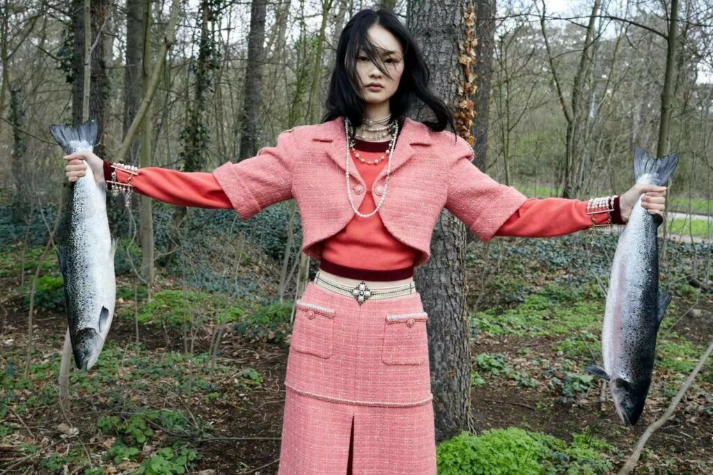 une jeune femme chinoise en élégant tailleur jupe rose propose au bout de ses bras tendus deux poissons de la forêt frais pêchés