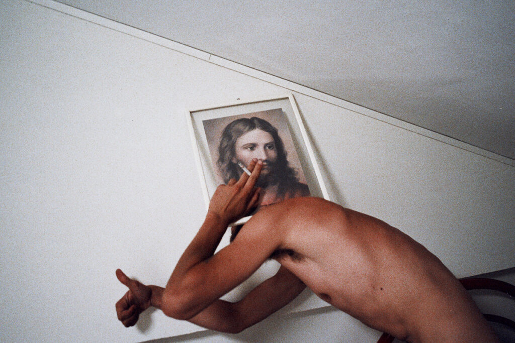 la photographie du christ sur un torse nu d'homme portant une cigarette à Sa bouche et faisant signe de l'autre main que tout va bien