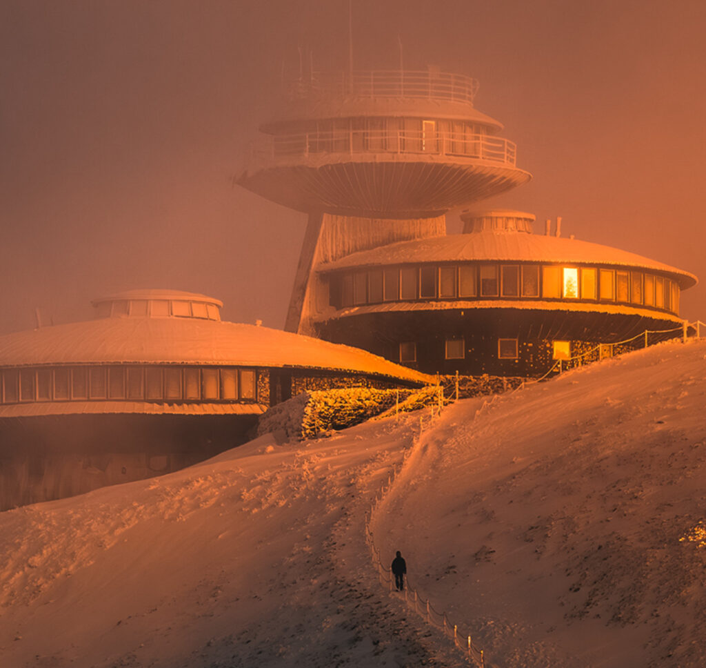 un homme se dirige dans la neige vers la frontière où des bâtiments circulaires sous le soleil levant sont posés comme des soucoupes volantes 