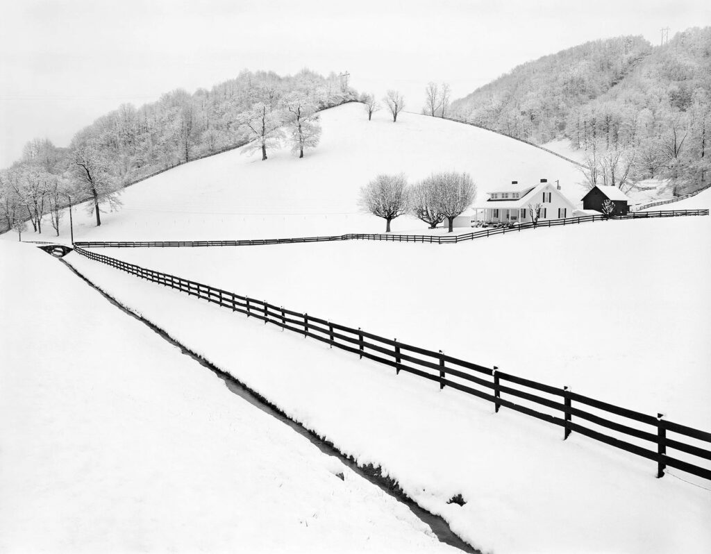 les lignes de fuite des barrières d'un champ attirant l'oeil vers un horizon excentré dans un paysage vallonné sous la neige