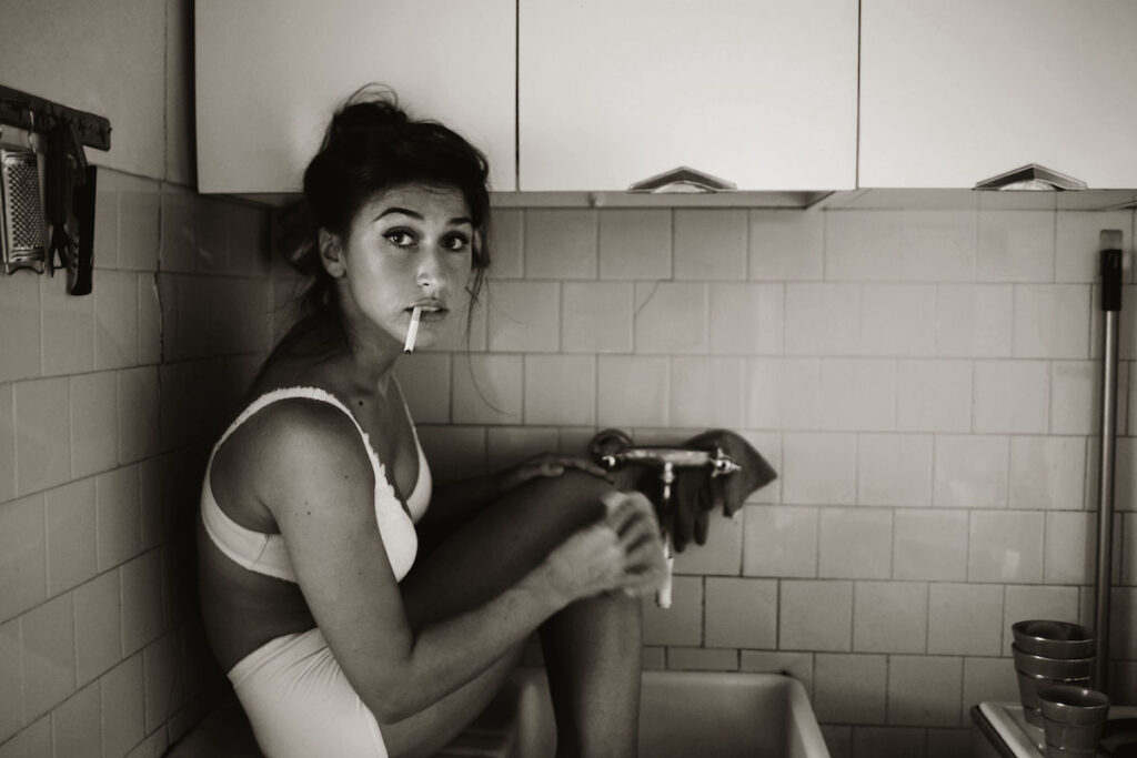 une femme brune en sous-vêtements blancs fait sa toilette dans l'évier de la cuisine