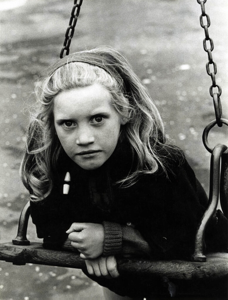 les avant-bras appuyés sur la balançoire, le regard profond d'une jeune fille sur le photographe 