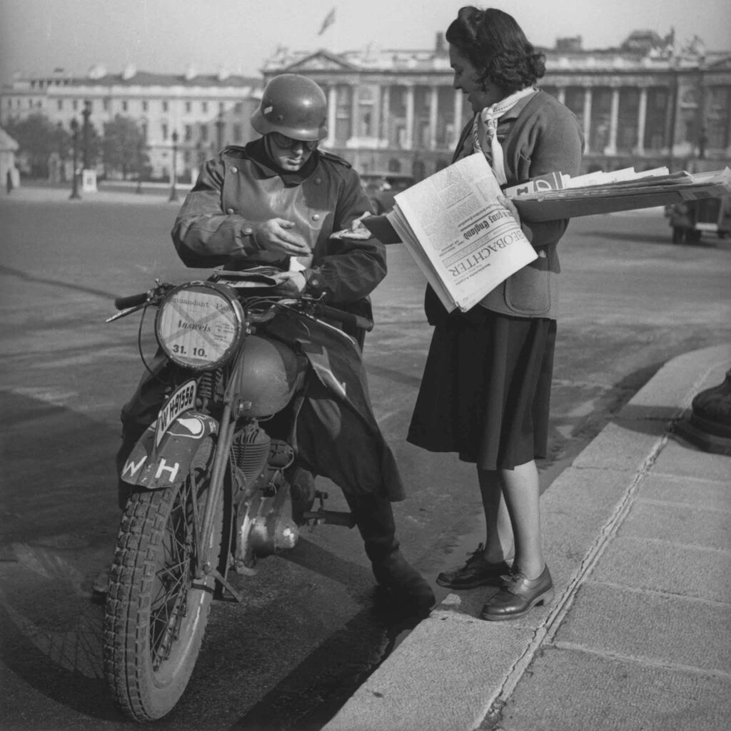 place de la Concorde, une jeune parisienne vend un journal en allemand à un soldat allemand à moto