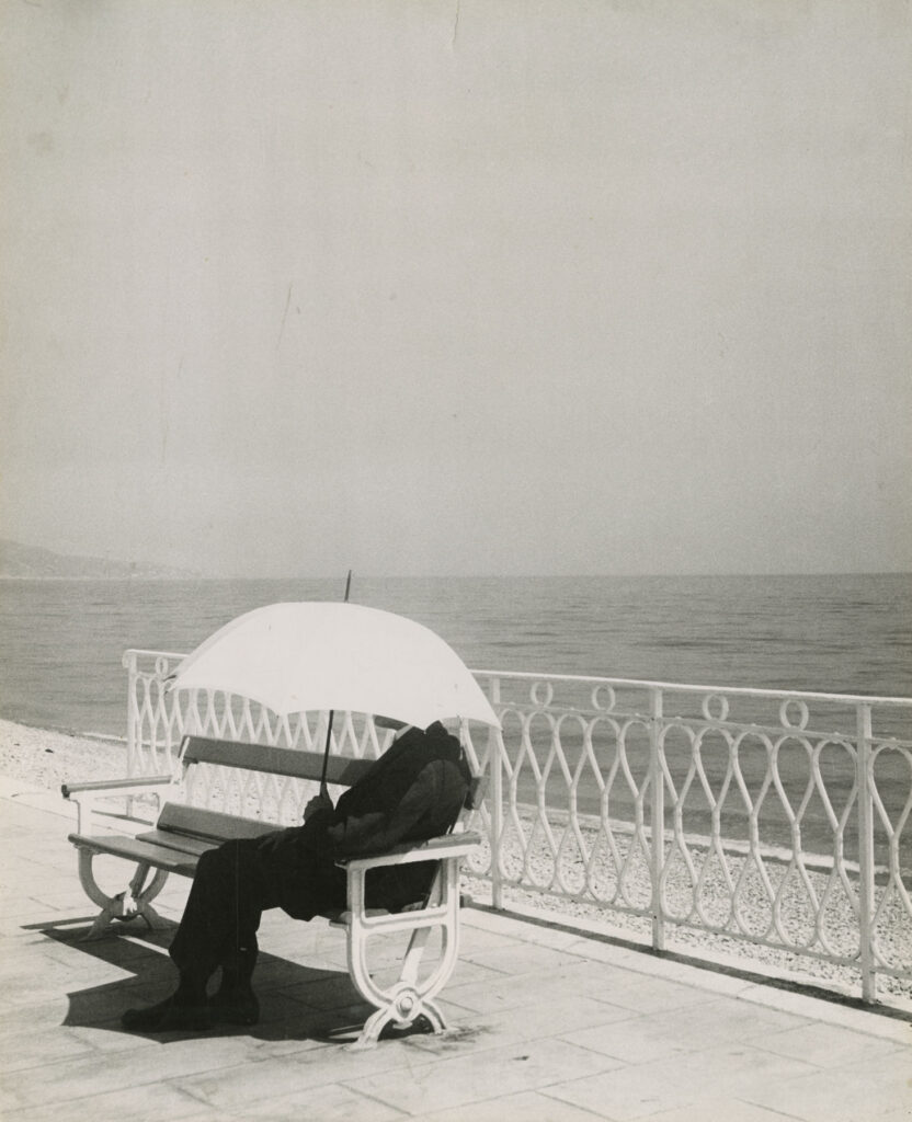 assis sous une ombrelle sur un banc public au bord de la mer, un homme est totalement protégé du soleil et d'autres évènements célestes potentiels