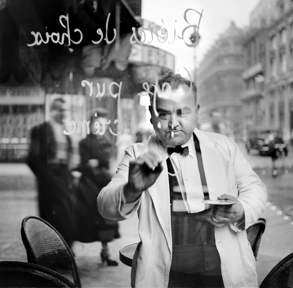 de l'autre côté de la vitre, un garçon de café écrit le menu du jour sur la vitrine