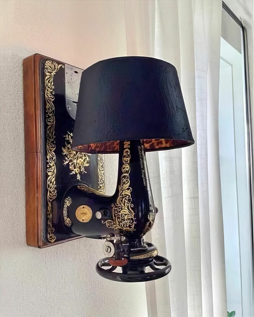 corps de machine à coudre Singer vintage transformée en applique murale, comme un mécanique bras noir aux arabesques d'or sortant du mur pour éclairer le monde, doté d'un élégant abat-jour en tissu uni