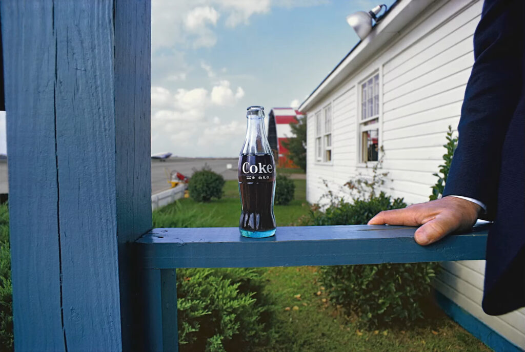 sur un porche bleu, le bras d'un homme en costume sombre et un coca noir