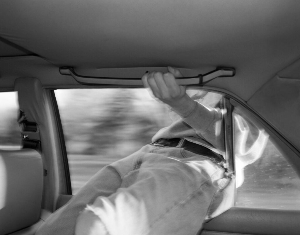 un homme passe le haut de son corps par la fenêtre d'une voiture en marche