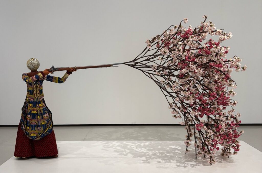 sculpture d'une figure féminine sans tête tirant des fleurs de cerisier avec un fusil 